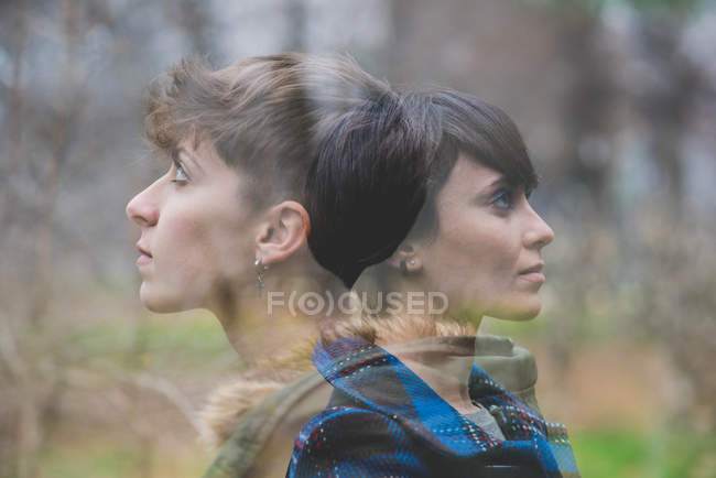 Dos mujeres jóvenes transparentes, espalda con espalda en el entorno rural - foto de stock