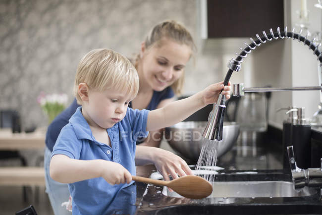 Mère aidant fils laver cuillère en bois — Photo de stock