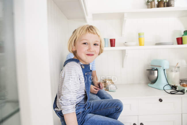 Портрет милой девушки, сидящей перед братом на кухонном столе — стоковое фото