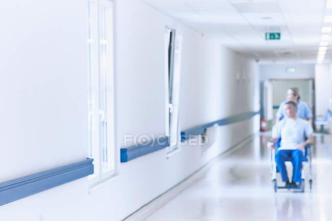 Медсестра штовхає пацієнта в інвалідне крісло вниз коридор — стокове фото