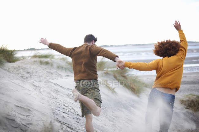 Casal correndo dunas de areia para a praia — Fotografia de Stock