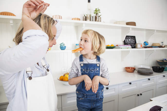 Mujer madura e hija imitando conejos con zanahorias en la cocina - foto de stock
