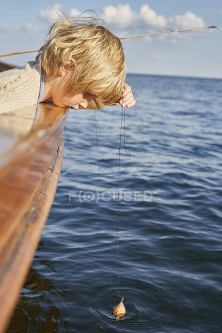 Ragazzo penzoloni pesca galleggiante dalla barca in blu oceano — Foto stock