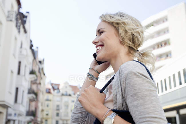 Mujer adulta paseando por la ciudad haciendo una llamada de teléfono inteligente - foto de stock