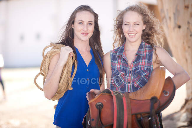 Young women carrying saddle and rope — Stock Photo