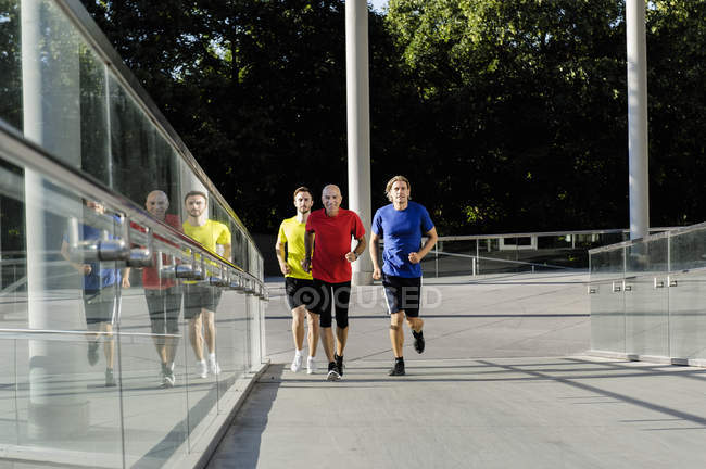 Male runners jogging alongside glass balustrade in city street — Stock Photo