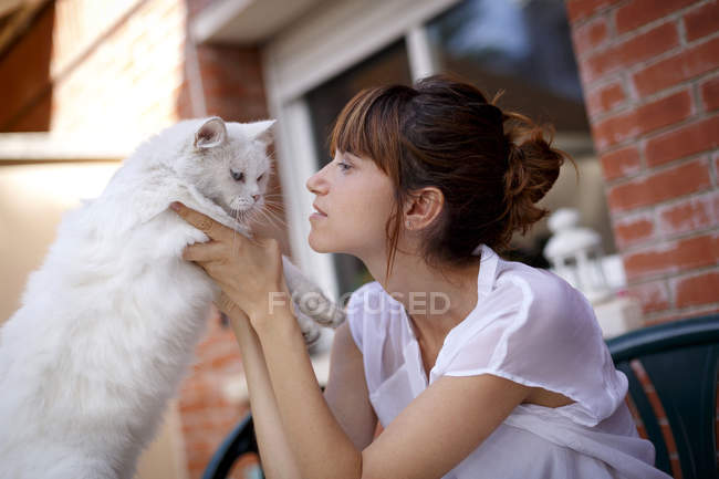 Femme adulte moyenne tenant un chat réticent sur le seuil de la porte — Photo de stock