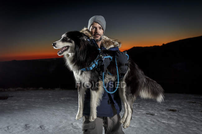 Retrato de hombre maduro llevando perro en la nieve por la noche - foto de stock