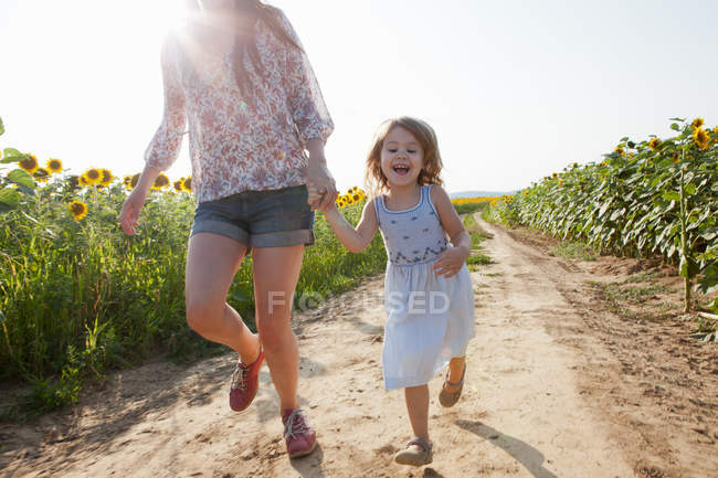 Mother and daughter running through field of sunflowers — Stock Photo