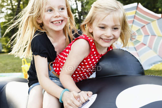 Two young sisters sitting on inflatable whale in park — Stock Photo