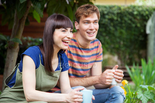 Couple laughing in garden with hot drinks — Stock Photo