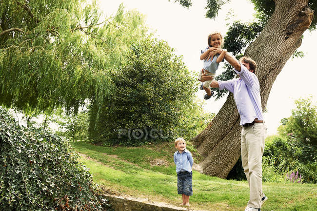 Зрілий чоловік піднімає дочку в саду — стокове фото
