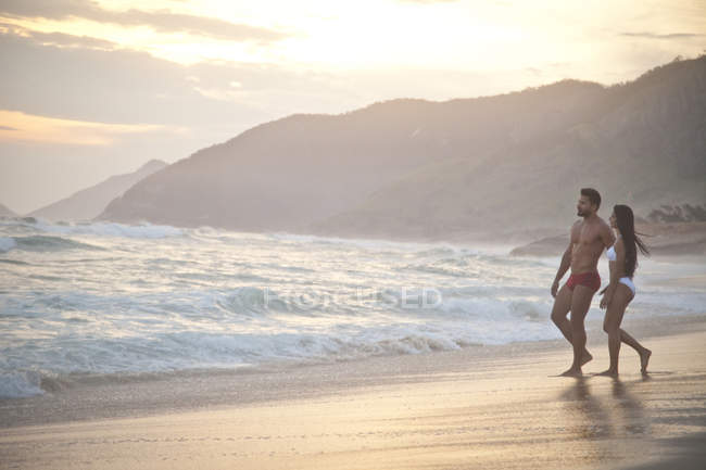 Взрослая пара на пляже, в купальниках, идущая к океану — стоковое фото