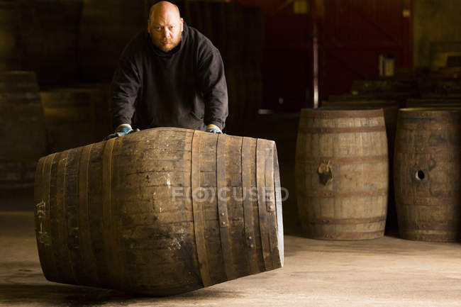 Porträt eines Arbeiters, der ein Whisky-Fass in einer Whisky-Brennerei rollt — Stockfoto