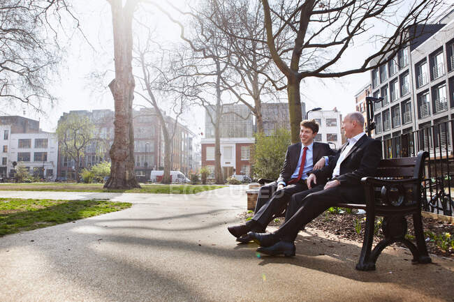Dos hombres de negocios sentados en el banco del parque - foto de stock