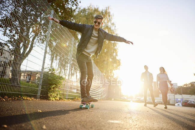 Joven skateboarder skateboarding masculino en la calle soleada - foto de stock