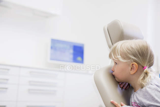 Fille assise à l'envers dans une chaise de dentiste regardant loin — Photo de stock