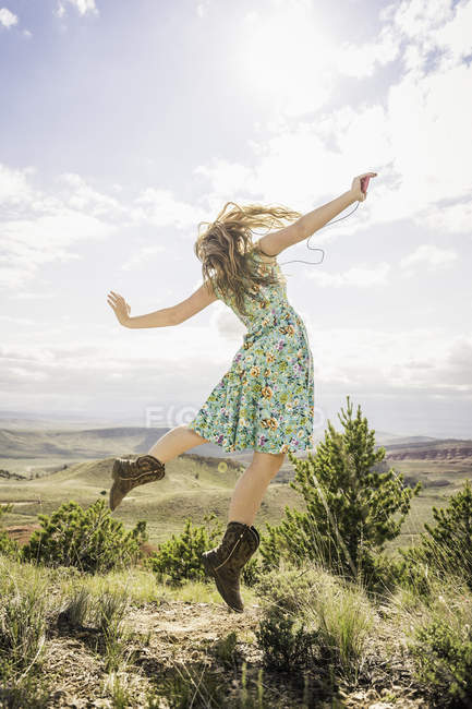 Young woman wearing dress and cowboy boots jumping in landscape, Bridger, Montana, USA — Stock Photo