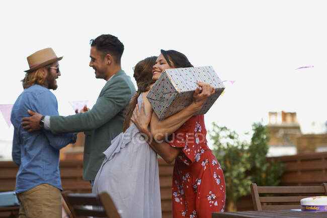 Couples meeting on roof terrace smiling, hugging holding gift — Stock Photo