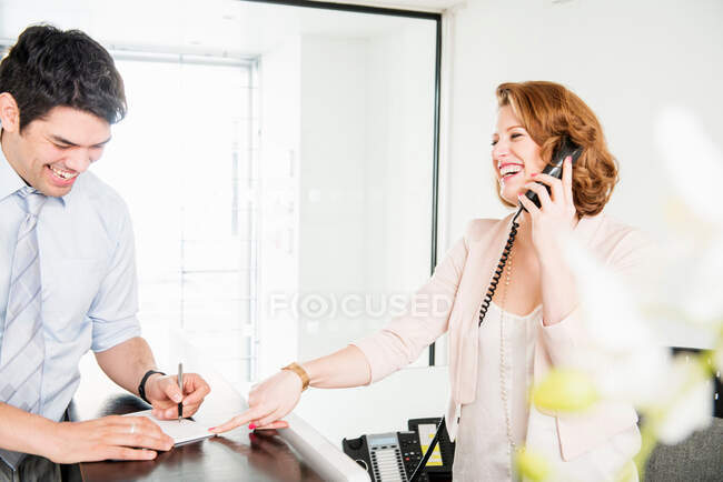 Man signing form at reception, woman on telephone — Stock Photo