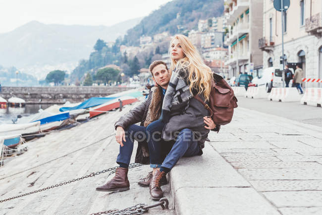 Jeune couple assis au bord du lac, Lac de Côme, Italie — Photo de stock