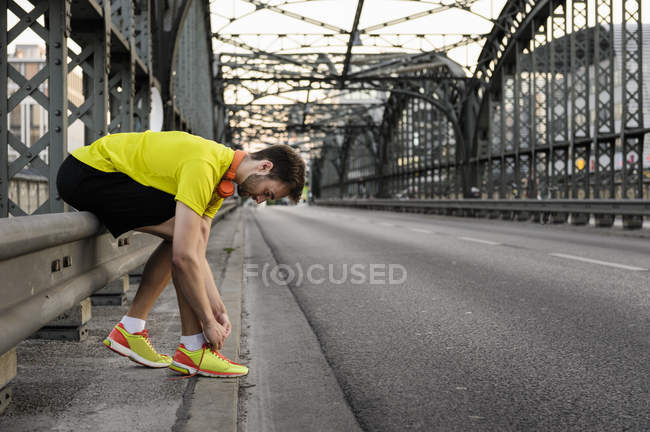 Giovane corridore maschile allacciatura lacci da scarpe sul ponte — Foto stock