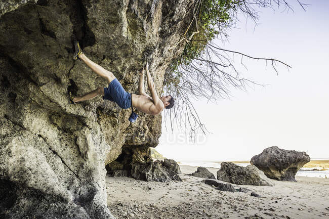 Male free climber climbing rock overhang on Pandawa Beach, Bali, Indonesia — Stock Photo