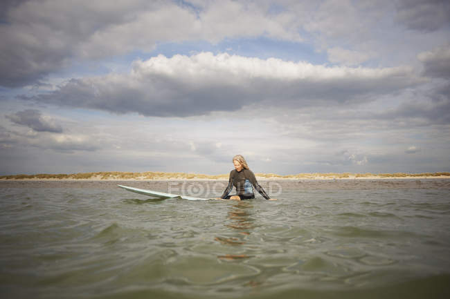 Senior woman sitting on surfboard in sea — Stock Photo