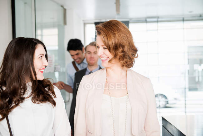Женщины-коллеги в офисном коридоре с мужчинами на заднем плане — стоковое фото