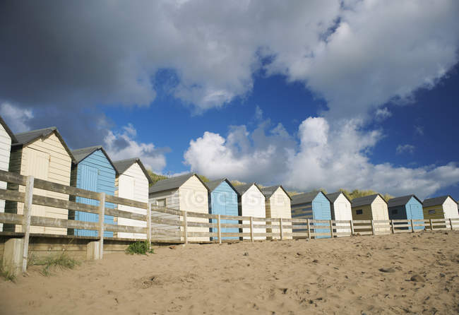 Fila di capanne da spiaggia blu e bianche sotto il cielo nuvoloso — Foto stock