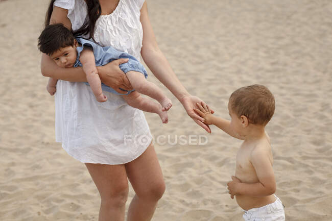 Madre llevando al bebé y tomándose de la mano con un niño pequeño - foto de stock
