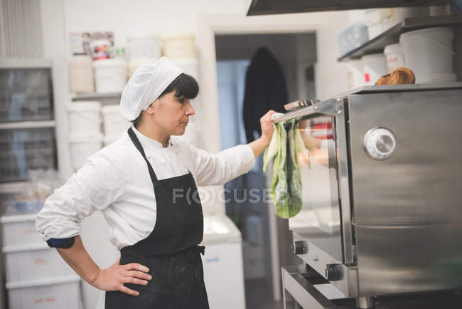 Fêmea padeiro olhando para forno na cozinha — Fotografia de Stock