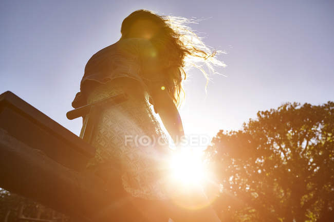 Девушка сидит на бензопиле, яркий солнечный свет светит сквозь деревья, вид с низкого угла — стоковое фото