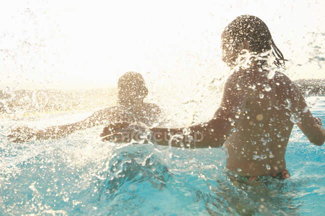 Casal se divertindo, salpicando na piscina ao ar livre — Fotografia de Stock