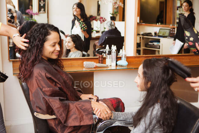 Girl and mother holding hands while having their hair styled in hair salon — Stock Photo
