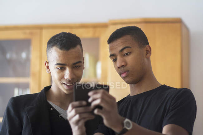 Hermanos gemelos en casa, mirando el teléfono inteligente - foto de stock