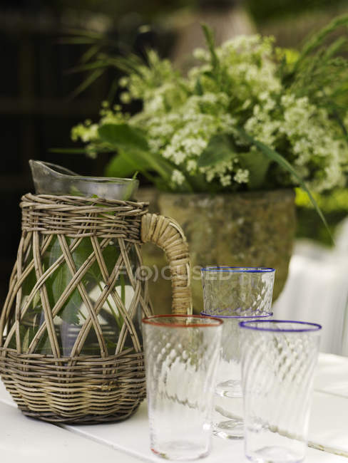 Винтажный плетеный кувшин и стаканы для питья на садовом столе — стоковое фото