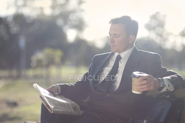 Hombre de negocios leyendo en el banco del parque - foto de stock