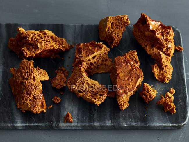 Broken honeycomb toffee on marble cutting board — Stock Photo