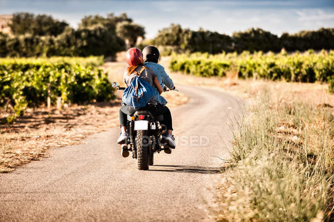 Вид сзади на среднюю взрослую пару, катающуюся на мотоцикле по извилистой сельской дороге — стоковое фото