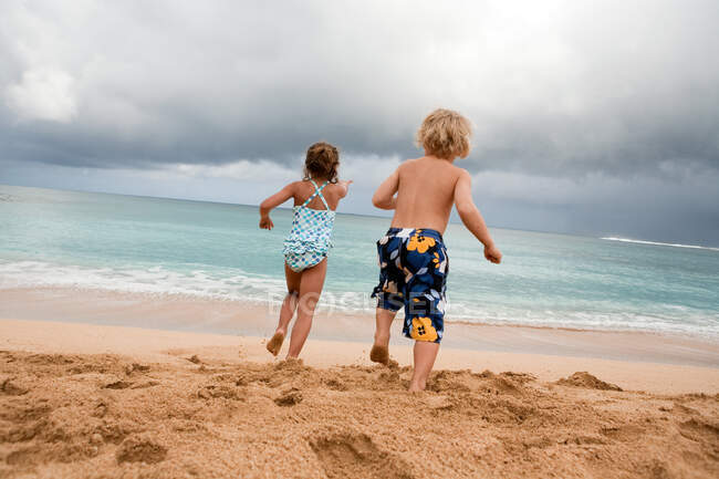 Niño y niña corriendo en la playa de arena - foto de stock