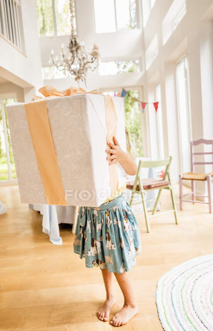 Waist down of girl at birthday party carrying large birthday present — Stock Photo