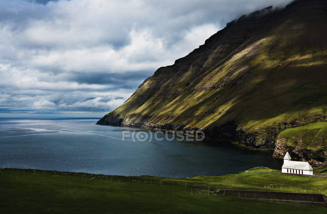 Lado de la montaña cubierta de hierba en la costa con cielo nublado - foto de stock