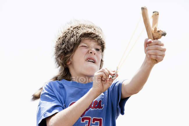 Мальчик в шляпе охотника играет с рогаткой — стоковое фото