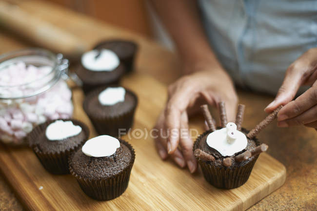 Hembra manos glaseado tortas de taza en la tabla de cortar - foto de stock