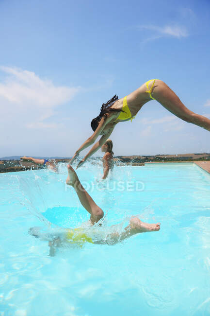 Four people jumping into swimming pool — Stock Photo