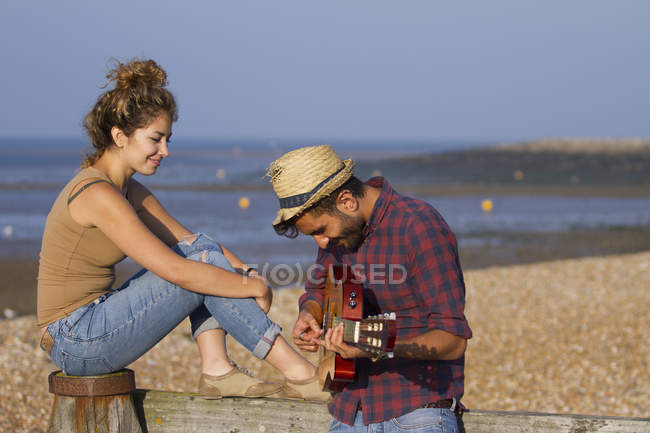 Молодая пара на пляже, мужчина играет на гитаре — стоковое фото