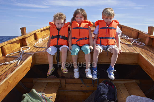 Three children in life jackets sitting in boat — Stock Photo