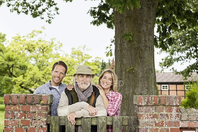 Portrait of senior man with mid adult couple leaning on gate — Stock Photo