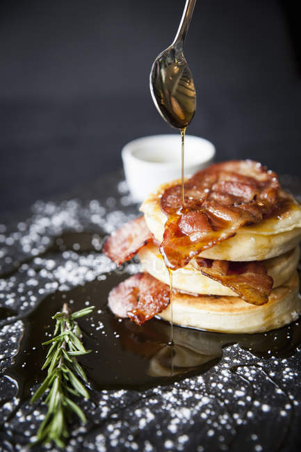 Breakfast bacon crumpet with maple syrup pouring from spoon onto slate — Stock Photo